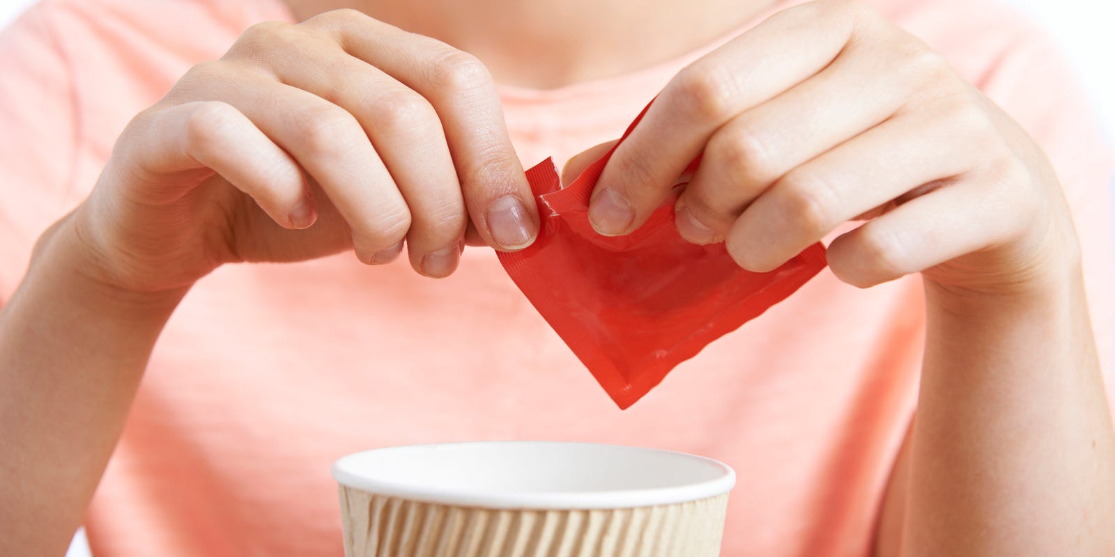 Person pouring artificial sweetener into a cup